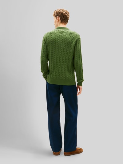 Männermodel trägt Regular Fit Strickpullover aus reiner Baumwolle von Tommy Hilfiger in Grün mit Zopfmuster, Ganzkörperansicht Rückansicht.
