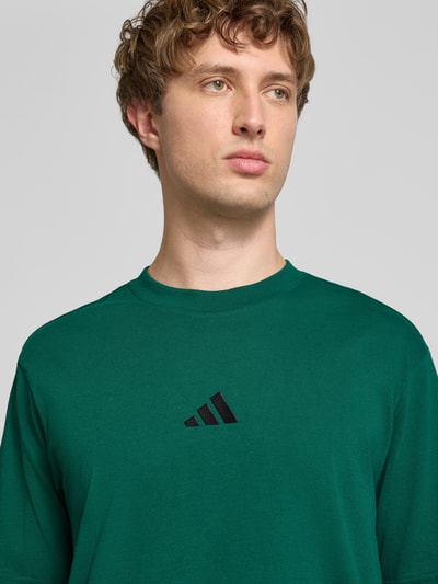 Männermodel trägt Regular Fit T-Shirt aus reiner Baumwolle von adidas Sportswear in groen met zwart logo, Nahaufnahme Oberkörper