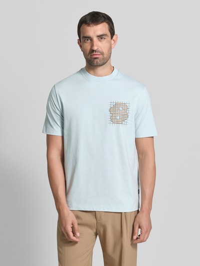 Mężczyzna nosi jasnoniebieski t-shirt model 'C-Tigerman 49' z bawełny od BOSS, beżowe spodnie, z przodu nadruk; Ganzkörperansicht von vorne. Męski t-shirt od BOSS.