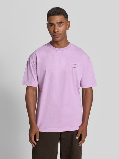 Männermodel trägt Oversized T-Shirt aus reiner Baumwolle Modell 'Joel' von Samsøe Samsøe in lila mit Logo-Print, rundhalsausschnitt, oversized fit, ganzkörperansicht von vorne.