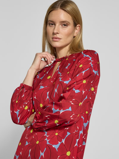 Frauenmodel trägt Tunikakleid aus Viskose mit Schlüsselloch-Ausschnitt von Luisa Cerano, rote Grundfarbe, Blumenmuster, Nahaufnahme Oberkörper, gerader Schnitt, knielang, blickdichtes Unterkleid, Rückseitiger Reißverschluss, lange Ärmel.