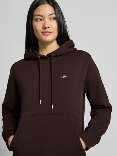 Frauenmodel trägt Regular Fit Hoodie aus Baumwoll-Mix von GANT in Dunkelbraun, weiche Struktur, dezentes Logo, Nahaufnahme Oberkörper. Damen Hoodie von GANT.
