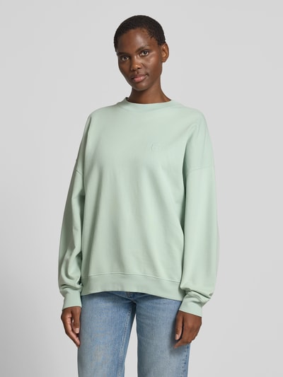 Frauenmodel trägt Oversized Sweatshirt mit Logo-Stitching von Anine Bing aus reiner Baumwolle im Oversized-Fit, Rundhalsausschnitt, elastische Abschlüsse, Rückenlänge bei Größe S 63 cm, hellgrün, glatte Oberfläche, Ganzkörperansicht von vorne.