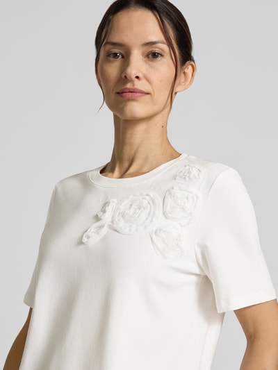 Modelka kobieca nosi Regular Fit T-Shirt mit floralem Besatz od Christian Berg Woman Selection, biały, okrągły dekolt, elastyczna bawełna, długość pleców w rozmiarze 36: 55 cm, zbliżenie na górną część ciała.
