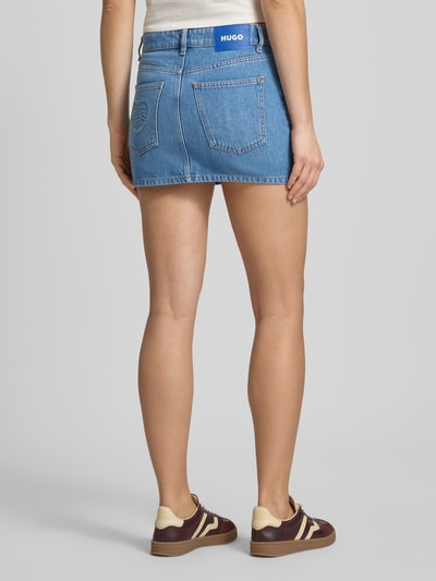 Frauenmodel trägt Regular Fit Jeansrock aus Baumwoll-Mix Modell 'GALANIE_B' von Hugo Blue in Blau, Denim-Optik, Mini-Länge, 5-Pocket-Design, Label-Patch, Ganzkörperansicht Rückansicht.