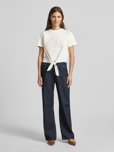 Frauenmodel trägt Regular Fit T-Shirt mit Lochmuster von Guess aus reiner Baumwolle mit Logo-Stitching und Rundhalsausschnitt, Ganzkörperansicht von vorne. Rückenlänge bei Größe S: 46 cm.