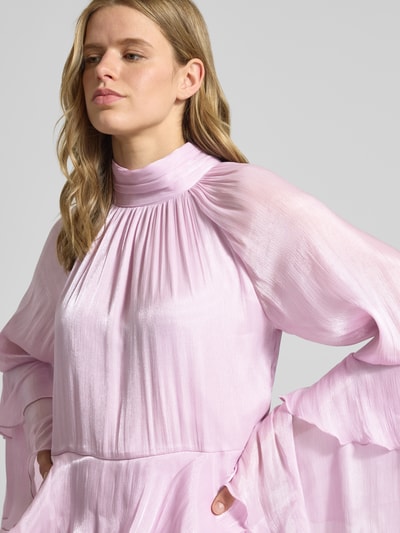 Frauenmodel trägt Minikleid im Stufen-Look Modell 'Flowy frill' von Gina Tricot in zartem Rosa mit Volants, Stehkragen und rückseitiger Schnürung, glatte und leicht glänzende Textur, Kontext: Damen Minikleid, A-Linie, Rückenlänge 91 cm, Brustweite 44 cm, Ärmellänge 61 cm, Nahaufnahme Oberkörper