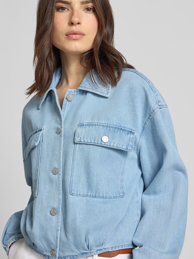 Modelka kobieca nosi kurtkę jeansową z mieszanki bawełny model 'Geviva' od mbyM, krój relaxed fit, listwa guzikowa, kieszenie na piersi, jasnoniebieska faktura, szerokość ramion w rozmiarze S: 56 cm, długość tyłu w rozmiarze S: 52 cm, szerokość klatki piersiowej w rozmiarze S: 55 cm, długość rękawów w rozmiarze S: 55 cm, zbliżenie na górną część ciała z przodu