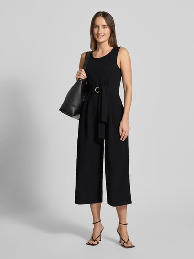 Kobiecy model nosi czarny Jumpsuit mit Rundhalsausschnitt od Apricot, taśma w talii, materiał z dodatkiem stretchu, widok całej sylwetki z przodu.