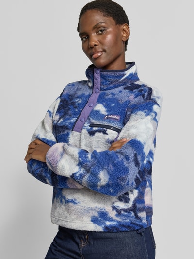 Vrouwenmodel draagt Fleeceshirt met opstaande kraag en labelpatch Model 'Helvetia II' van Columbia in blauw-wit Fleece, straight fit, borstzak met ritssluiting, drukknopen, detailopname bovenlichaam.