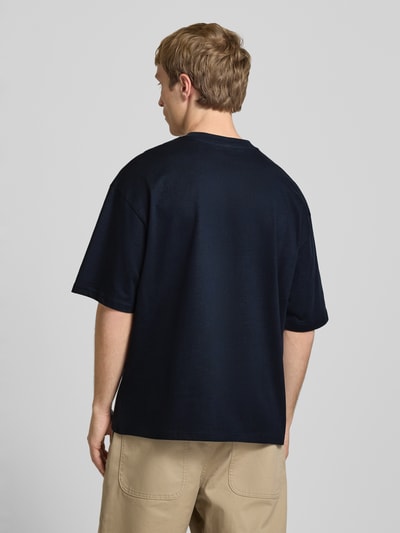 Männermodel trägt Oversized T-Shirt mit Logo von REVIEW aus Reine Baumwolle, dunkle Farbe, Rückenlänge 70 cm, Ganzkörperansicht Rückansicht.