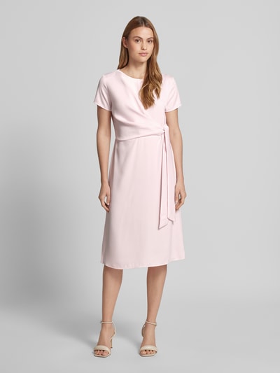 Frauenmodel trägt knielanges Cocktailkleid mit Knotendetail und Reißverschluss von Rinascimento in zartem Rosa, Taillierter Schnitt, Rundhalsausschnitt, glatte Oberfläche, Ganzkörperansicht von vorne, Rückenlänge 105 cm, Brustweite 46 cm, Ärmellänge 17 cm bei Größe S.