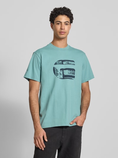 Männermodel trägt Regular Fit T-Shirt mit Logo-Print Modell 'icon' von G-Star Raw in Hellblau, reine Baumwolle, Ganzkörperansicht von vorne.