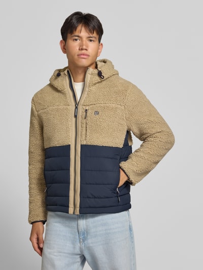 Męski model nosi Regular Fit Jacke mit Teddyfell Modell 'Borg' od Superdry, beż i granat, kaptur z troczkiem, kieszeń napoleonka i boczne, kurtka z teksturą pluszu, długość pleców 64 cm, szerokość ramion 45 cm, szerokość klatki piersiowej 55 cm, długość rękawa 68 cm, zdjęcie całej sylwetki z przodu.