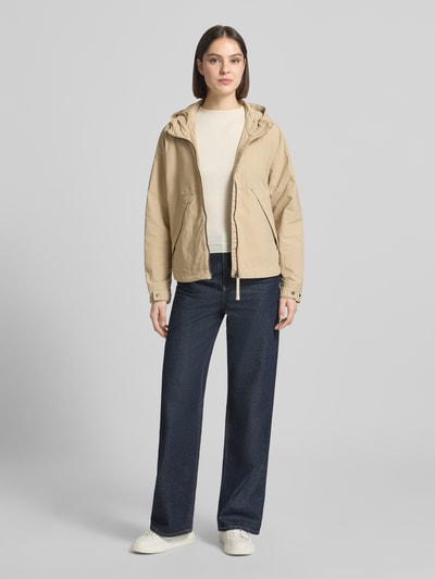Frauenmodel trägt Jacke mit Kapuze und Zweiwege-Reißverschluss von camel active in Beige, Gerader-Schnitt, Eingrifftaschen. Ganzkörperansicht von vorne. Rückenlänge 67 cm, Schulterbreite 44 cm, Brustweite 63 cm, Ärmellänge 62 cm bei Größe 36.
