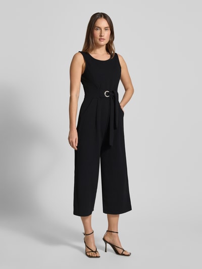 Modelka kobieca nosi czarny Jumpsuit mit Rundhalsausschnitt od Apricot, materiał z dodatkiem stretchu, taliowany krój, widok całej sylwetki z przodu.