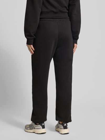 Frauenmodel trägt Basic Sweatpant mit Bündchen am Saum und seitlichen Taschen von Review, schwarzer Baumwoll-Mix, lockere Passform, Logo-Stickerei, elastische Abschlüsse, Label-Print, Innenbeinlänge bei Größe S: 74 cm, Ganzkörperansicht Rückansicht.