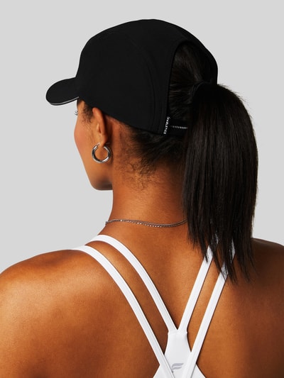 Frauenmodel trägt schwarze Base Cap mit Logo-Stitching Modell 'The Fundamental Ponytail' von Fabletics, elastischer Material-Mix, Ganzkörperansicht Rückansicht.