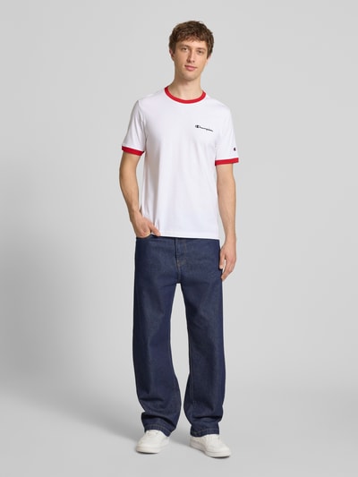 Männermodel trägt T-Shirt mit Rundhalsausschnitt und Label-Stitchings von CHAMPION, Weiß mit roten Details, Reine Baumwolle, Regular-Fit, Herren T-Shirt, Rückenlänge bei Größe M 70 cm, Ganzkörperansicht von vorne.