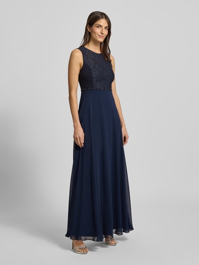 Frauenmodel trägt Regular Fit Abendkleid mit floralem Spitzenbesatz von Jake*s Cocktail in Dunkelblau, semitransparent mit Pailetten, Ganzkörperansicht von vorne.