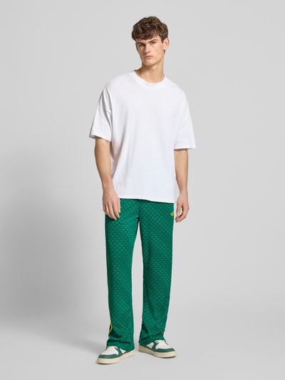 Männermodel trägt grüne Sweatpants mit elastischem Bund von adidas Originals, lockerer Schnitt, Eingrifftaschen, Label-Stitching, Ganzkörperansicht von vorne.