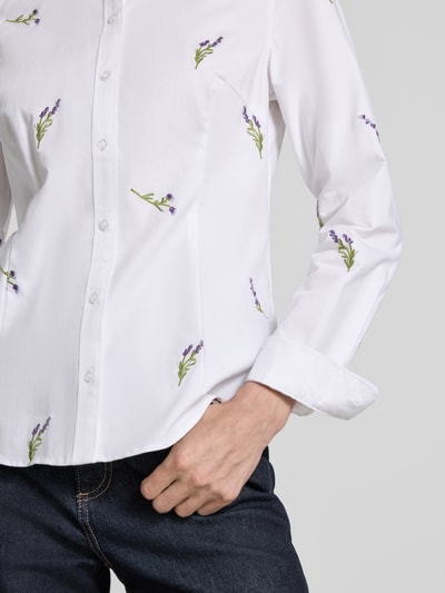 Kobieta nosi Hemdbluse mit Motiv-Stitchings od Christian Berg Woman, biała bawełna, motywy haftowane, prosty krój, zbliżenie na górną część ciała.