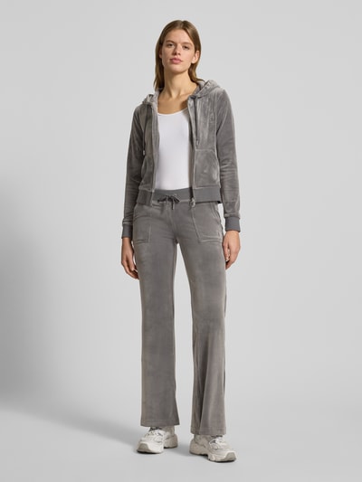 Frauenmodel trägt Low Rise Sweatpants mit elastischem Bund Modell 'LAYLA' von Juicy Couture aus grauem Baumwoll-Mix mit Stretch-Anteil, Flared-Cut, Eingrifftaschen, Ganzkörperansicht von vorne.