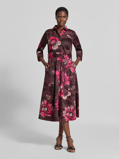 Frauenmodel trägt Midikleid aus reiner Baumwolle von Christian Berg Woman mit floralem Allover-Print, dunkle und pinke Töne, Ganzkörperansicht von vorne. Taillierte Passform, Umlegekragen, integriertes Taillenband, 1/2-Arm, glatte Textur, Rückenlänge 123 cm, Brustweite 50 cm, Ärmellänge 47 cm.