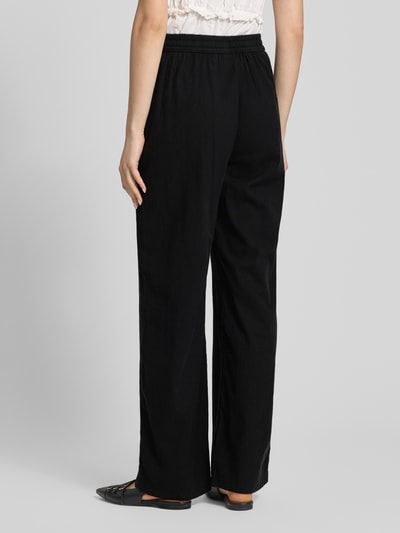 Frauenmodel trägt Wide Fit Stoffhose mit elastischem Bund Modell 'Poppy' von JJXX, schwarz, glatte Struktur, Ganzkörperansicht Rückansicht.