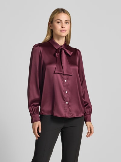 Vrouwenmodel draagt Regular Fit Hemdbluse aus Satin van Christian Berg Woman Selection, bordeauxrood met glanzende satijntextuur, sierstrik, hemdkraag, lange mouwen, voorkant volledig zichtbaar, Ganzkörperansicht von vorne.