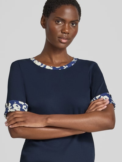 Frauenmodel trägt T-Shirt mit Rundhalsausschnitt und Ärmeln mit Aufschlag von Marc Cain in Dunkelblau, Nahaufnahme Oberkörper, Baumwoll-Elasthan-Mix, Slim Fit, Label-Detail, Rückenlänge 54 cm bei Größe 36.