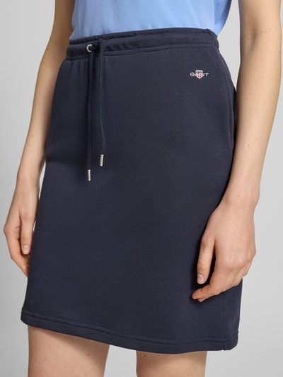 Vrouwenmodel draagt Sweatrock met Label-Stitching van Gant, katoenmix, recht model, minirok, elastische band met tunnelkoord, donkerblauw, detailopname, bandwijdte maat S 37 cm, totale lengte maat S 52 cm.