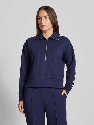 Frauenmodel trägt Sweatshirt mit kurzem Reißverschluss von Christian Berg Woman in Dunkelblau, Material-Mix mit Modal-Anteil, Umlegekragen, lockerer Schnitt, gerippte Abschlüsse, Ganzkörperansicht von vorne.