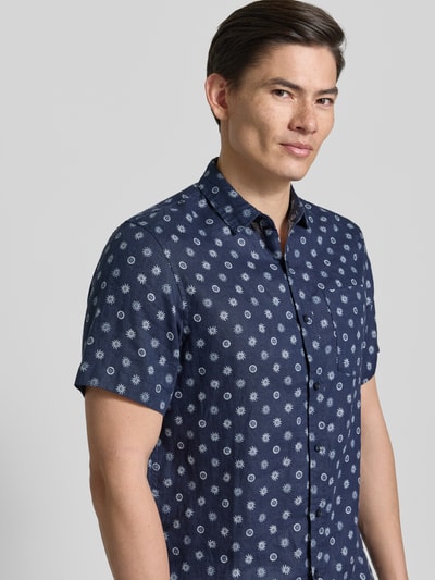 Männermodel trägt Regular Fit Leinenhemd mit Brusttasche von Scotch & Soda, Reine Leinen, Kentkragen, Allover-Motiv-Print, Kurzärmelig, Logo-Patch, durchgehende Knopfleiste, Nahaufnahme Oberkörper.