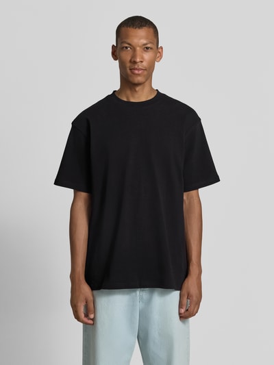 Männermodel trägt schwarzes Relaxed Fit T-Shirt aus reiner Baumwolle Modell 'MAARKOS' von ARMEDANGELS, Ganzkörperansicht von vorne.