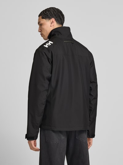 Męskimodel nosi Midlayer kurtkę ze stójką model 'CREW' od Helly Hansen, prosty krój, czarna, gładka tekstura, pełny tył. Ganzkörperansicht Rückansicht. Szerokość ramion w rozmiarze M: 49 cm, szerokość w rozmiarze M: 52 cm, długość tyłu w rozmiarze M: 74 cm, długość rękawów w rozmiarze M: 68 cm, kieszenie zapinane na zamek błyskawiczny, nadruk z logo.