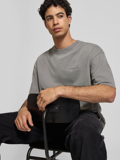 Männermodel trägt Oversized T-Shirt mit Label-Stitching von Pegador aus reiner Baumwolle, gerippter Rundhalsausschnitt, Nahaufnahme Oberkörper.