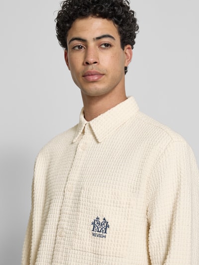 Männermodel trägt Regular Fit Freizeithemd mit Logo-Stitching von REVIEW in Creme mit Strukturmuster, reine Baumwolle, Nahaufnahme Oberkörper.