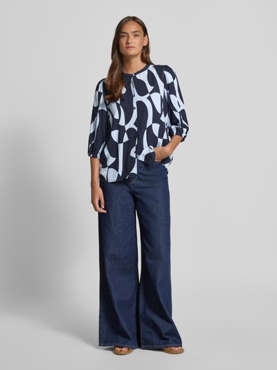 Kobiece modelka nosi Regular Fit bluzkę z wiskozy z rękawem o dł. 3/4 model 'CHANISE' od Soyaconcept, wzór na całej powierzchni, okrągły dekolt, długość tyłu w rozmiarze S 64 cm, długość rękawów 45 cm, granatowo-białe odcienie, gładka tekstura, widok całej sylwetki z przodu.