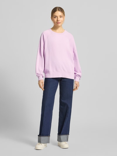 Frauenmodel trägt Sweatshirt mit stark überschnittenen Schultern Modell 'ATUBAY' von American Vintage in Hellviolett, lockerer Schnitt, Baumwoll-Mix, Rundhalsausschnitt, kombiniert mit blauer Jeans, Ganzkörperansicht von vorne.