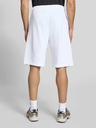 Männermodel trägt Shorts mit Logo-Print und -Stitching von CHAMPION, weiß, lockerer Schnitt, Baumwoll-Mix, Ganzkörperansicht Rückansicht.