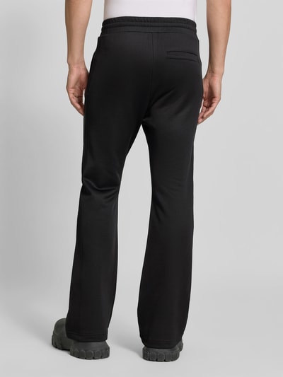 Männermodel trägt schwarze Flared Fit Hose aus Baumwoll-Mix von Diesel mit Gesäßtasche und elastischem Bund, Ganzkörperansicht Rückansicht.