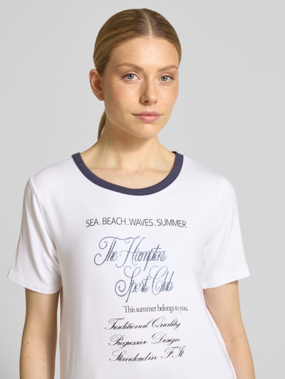 Frauenmodel trägt Damen T-Shirt aus Viskose-Mix Modell 'Hamptons Spirit' von monari in Weiß mit Kontrast-Rundhalsausschnitt, Nahaufnahme Oberkörper, Gerader-Schnitt, 1/2-Arm, Rückenlänge 51 cm in Größe 36.