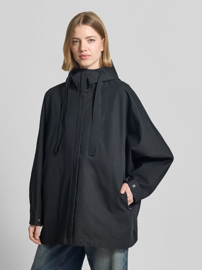 Modelka kobieca nosi kurtkę Jacke mit Kapuze und Eingrifftaschen Modell 'FEEL' od G-LAB z mieszanki bawełny, luźny krój, kaptur z trokiem, wpuszczane kieszenie, zapięcie na zamek błyskawiczny kryty, regulowane patki przy mankietach na zatrzaski, długość tyłu w rozmiarze S: 78 cm, szerokość ramion w rozmiarze S: 49 cm, szerokość klatki piersiowej w rozmiarze S: 84 cm, długość rękawa w rozmiarze S: 58 cm, kolor ciemny, prosta tekstura, gładki materiał, widok całej sylwetki z przodu.