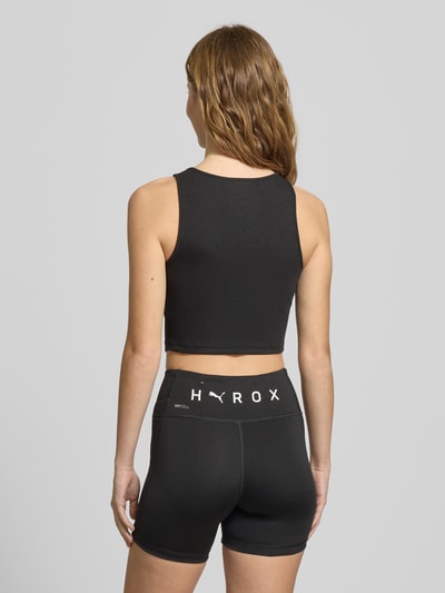 Frauenmodel trägt schwarzes PUMA x HYROX - Crop Top mit Label-Stitching aus Baumwoll-Mix, Slim Fit, Rückenlänge 35 cm, Ganzkörperansicht Rückansicht.