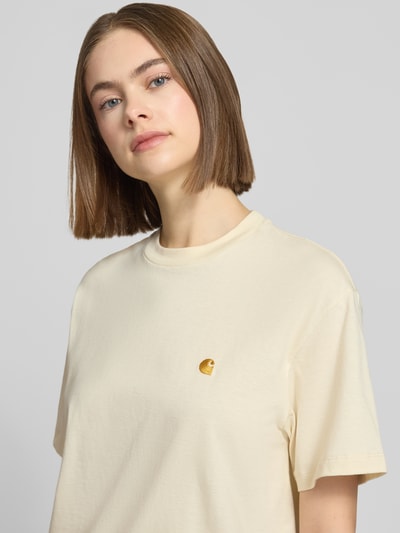 Frauenmodel trägt T-Shirt mit Label-Stitching von Carhartt Work In Progress in Creme, Bio-Baumwolle, Rundhalsausschnitt, Nahaufnahme Oberkörper.