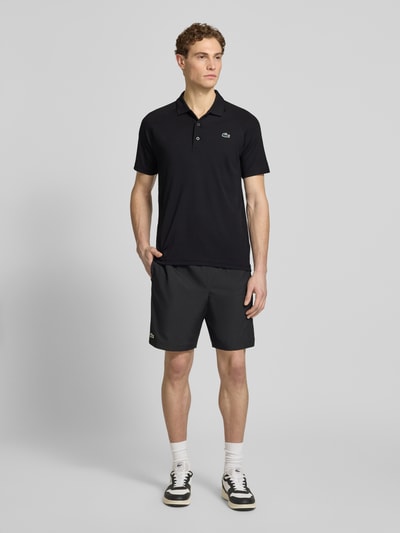 Männermodel trägt Regular Fit Sport Poloshirt mit Label Patch von Lacoste Sport in Schwarz, kurzarm, unifarben, Piqué, Ganzkörperansicht von vorne.