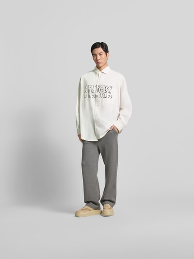 Männermodel trägt Relaxed Fit Freizeithemd mit Brusttasche von MM6 Maison Margiela in Weiß mit schwarzem Print, Kentkragen, Baumwolle, Ganzkörperansicht von vorne.