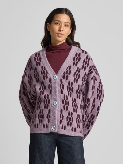 Vrouwenmodel draagt Strickjacke mit Knopfleiste Modell 'VITOW' van American Vintage, mix van alpaca en lanawol met stretch, los model, ribboorden, V-hals, knoopsluiting, lengte rug 67 cm, mouwlengte 53 cm, paarse tinten met donkere vlekken, grof gebreid, Ganzkörperansicht van voren.