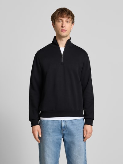 Männermodel trägt Regular Fit Sweatshirt mit Troyer-Kragen Modell 'Bradley' von Jack & Jones in Schwarz, Ganzkörperansicht von vorne, Material-Mix mit Baumwoll-Anteil, elastische Abschlüsse.